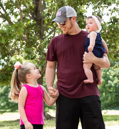 Father holding his infant daughter and young daughter's hand outside