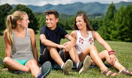 Two young girls and a young boy smiling and sitting together in a field